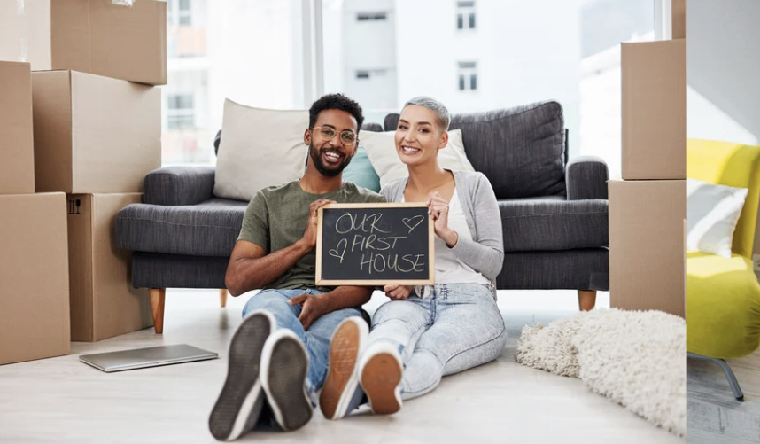 Happy couple standing outside their new home holding a “Our First Home” sign, celebrating their real estate purchase in St. Petersburg, Florida.